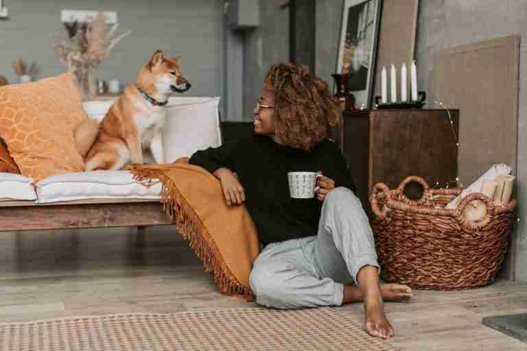 Relaxed woman with Shiba Inu dog enjoying cozy home ambiance, sipping coffee indoors.