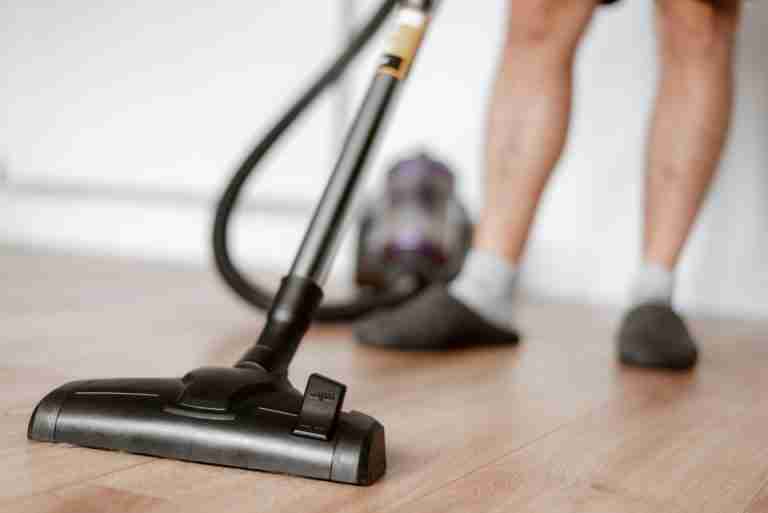 Crop anonymous male in slippers washing floor with vacuum cleaner in flat during household routine